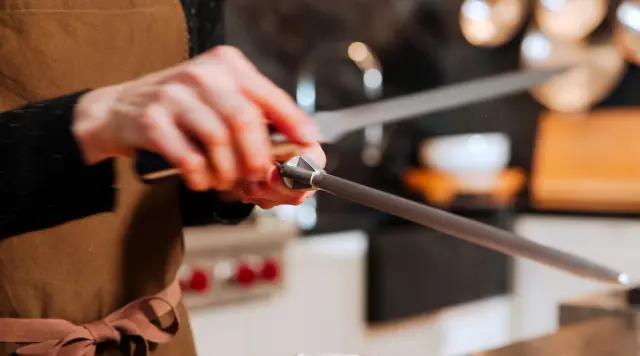 A person sharpens a knife on a honing steel in a kitchen setting.