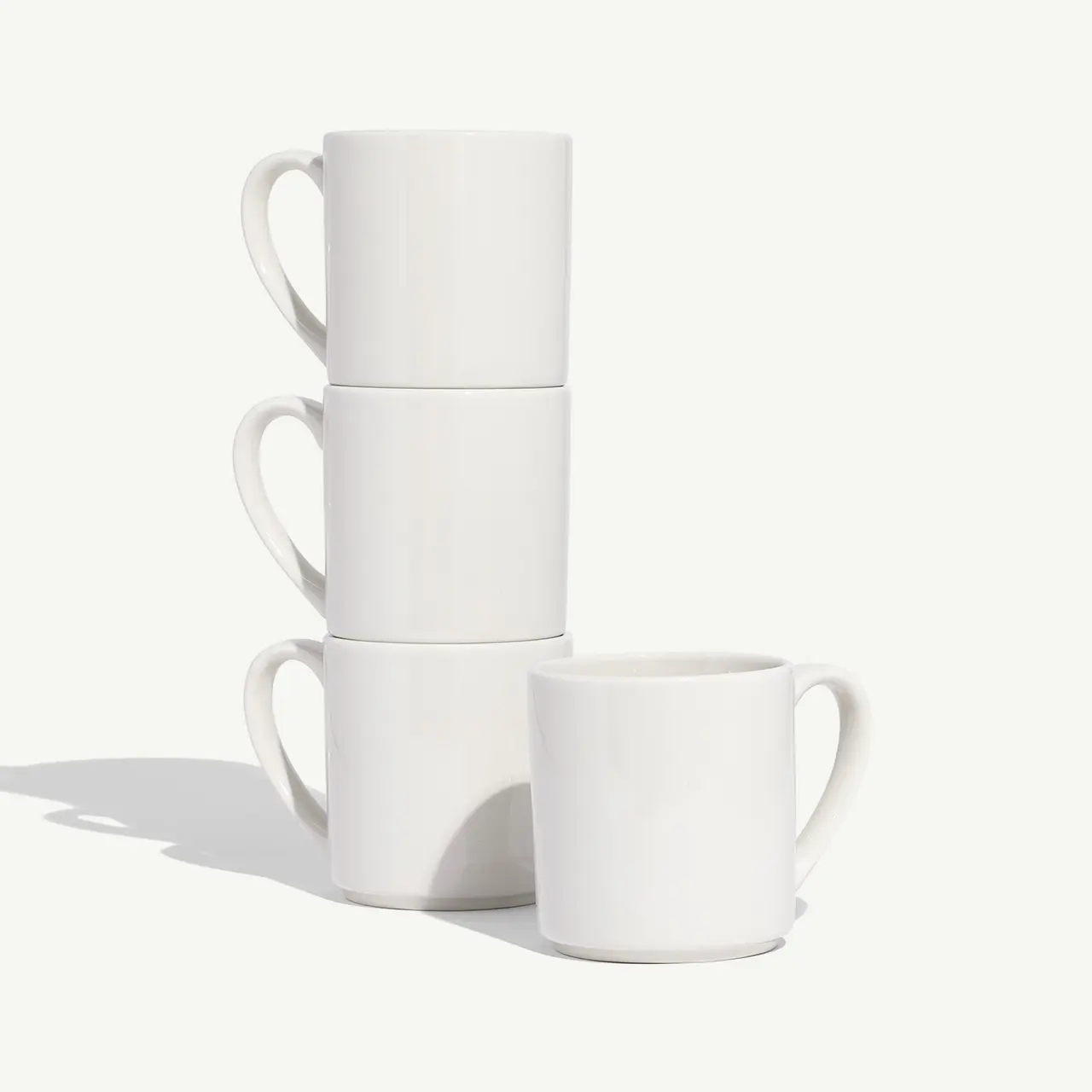 Three white coffee mugs are stacked on top of each other with one laying on its side in front on a plain background.