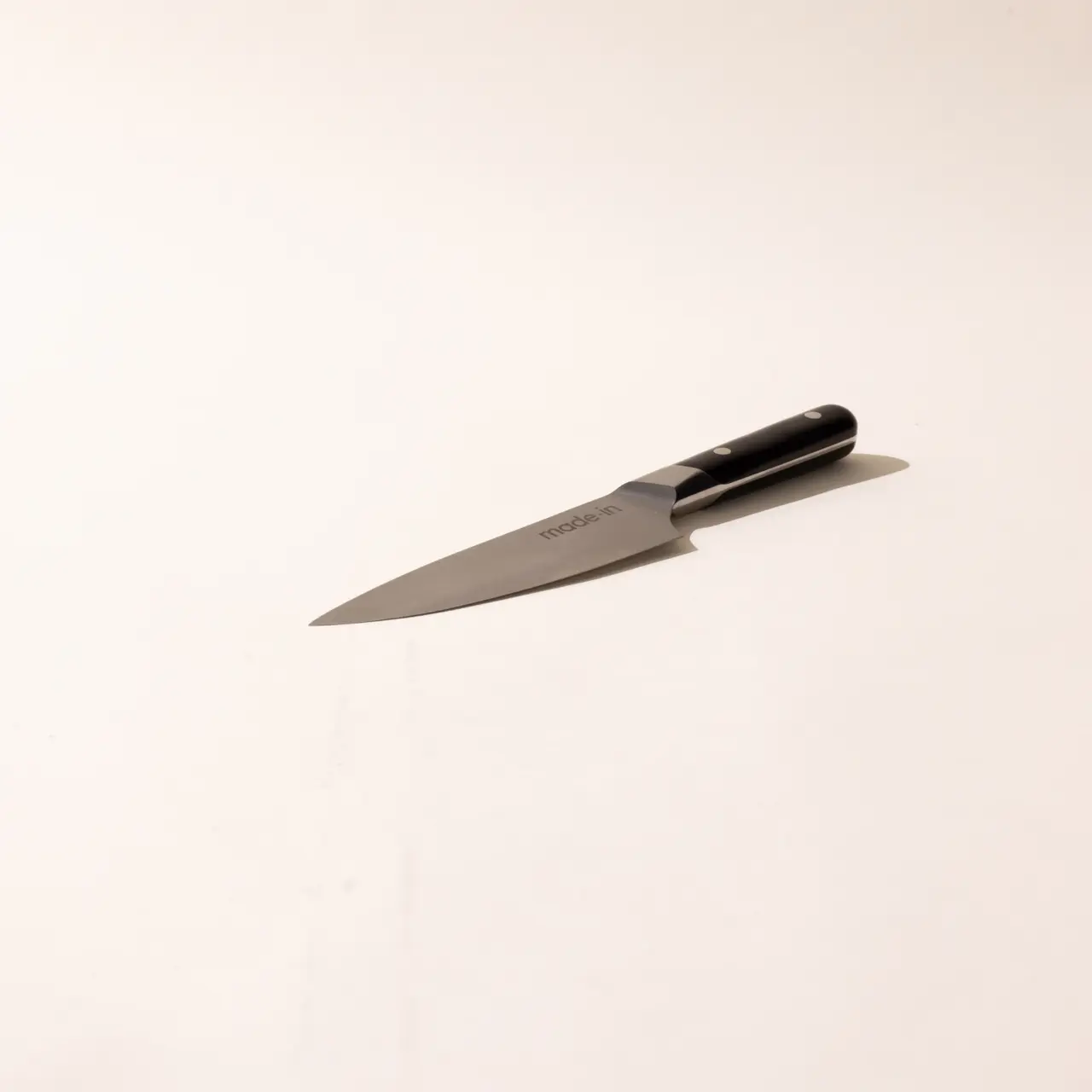 A solitary kitchen knife with a black handle is lying flat on a plain light background.