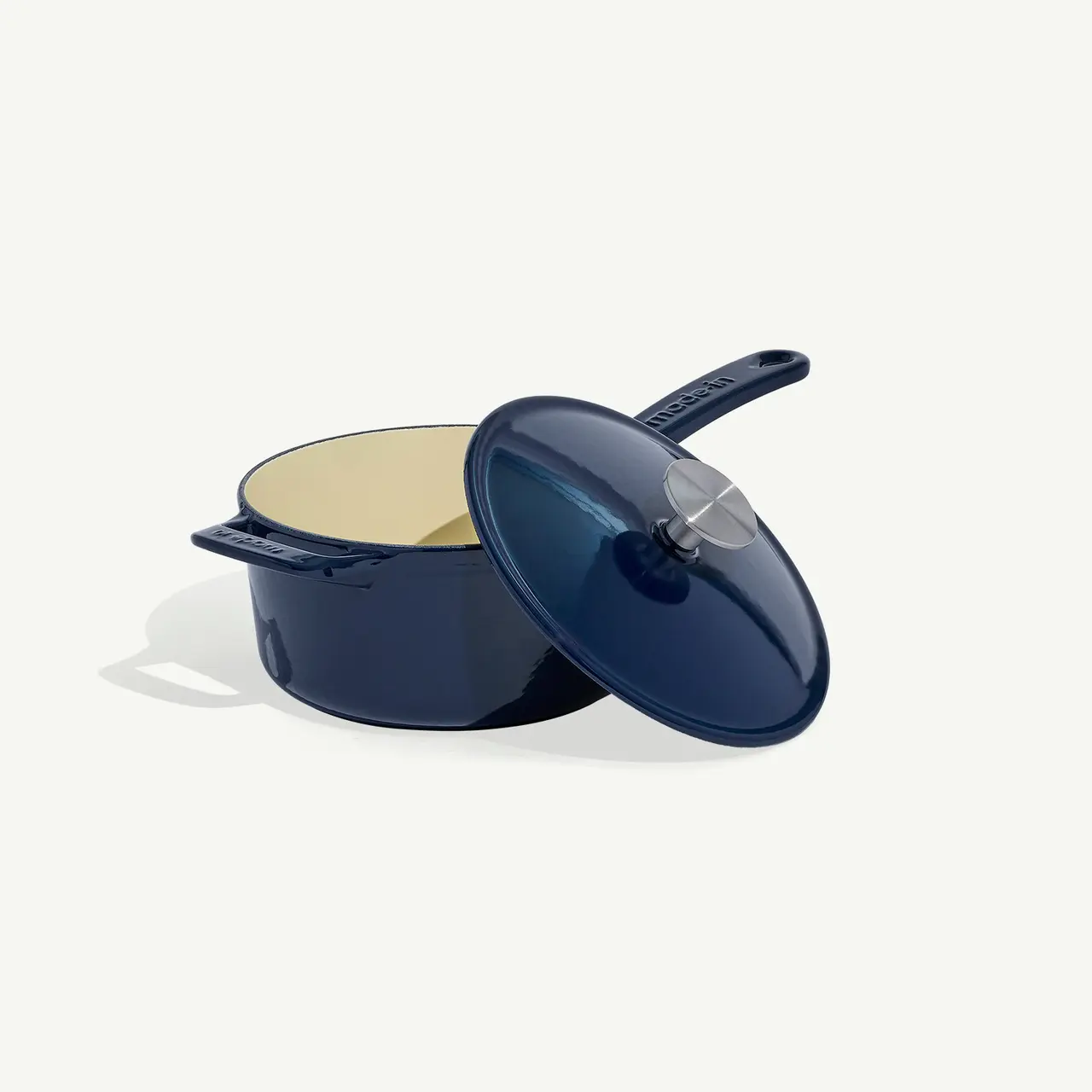 A navy blue enameled saucepan with a matching lid set askew, resting on a light background.