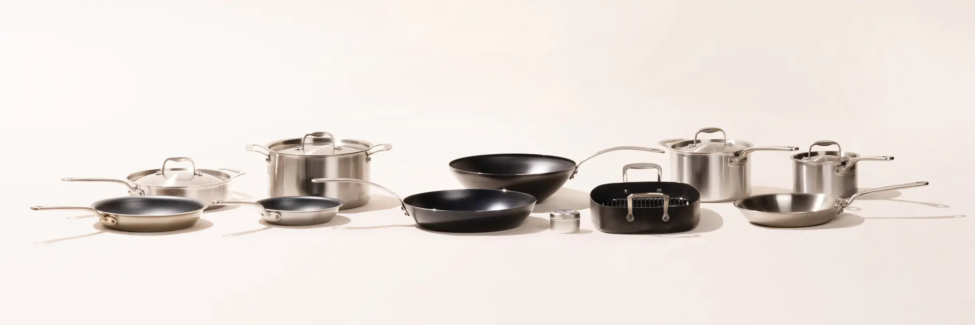 A variety of stainless steel and non-stick cookware including pots and pans with lids spread out on a light background.