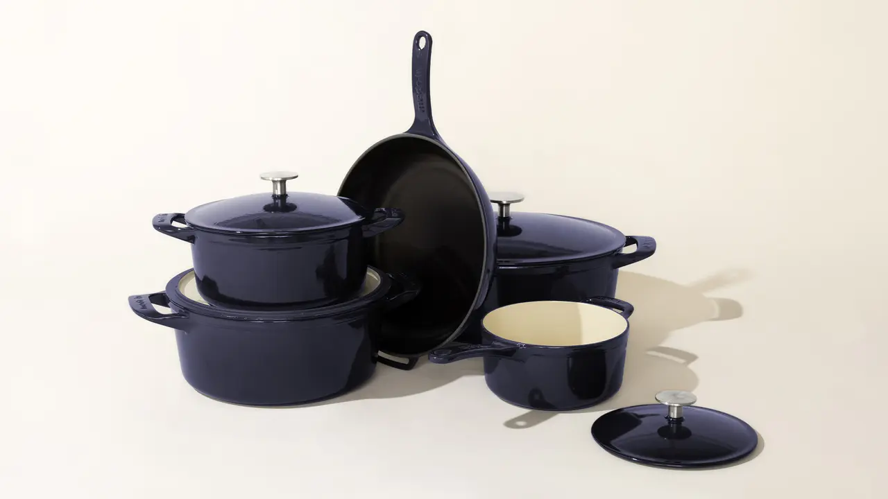 A set of dark-colored kitchen cookware consisting of pots with lids and a frying pan, arranged on a light surface.
