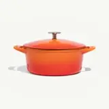 A vibrant orange Dutch oven with a lid is centered on a light background.