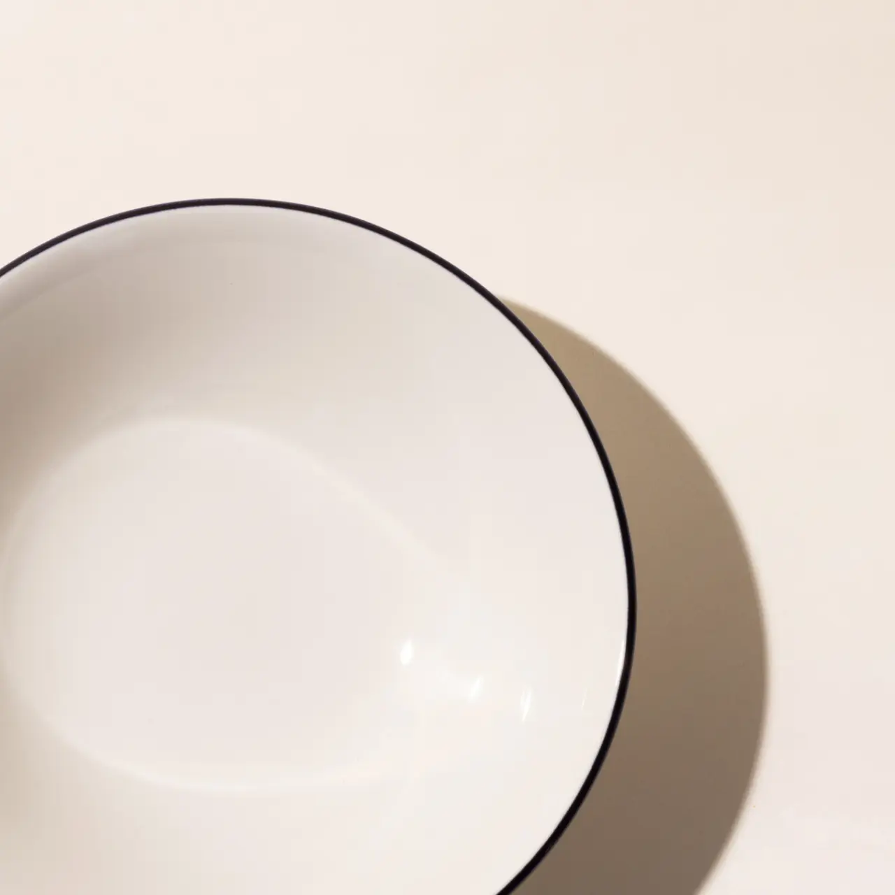 A simple white bowl with a blue rim, casting a shadow on a light surface.