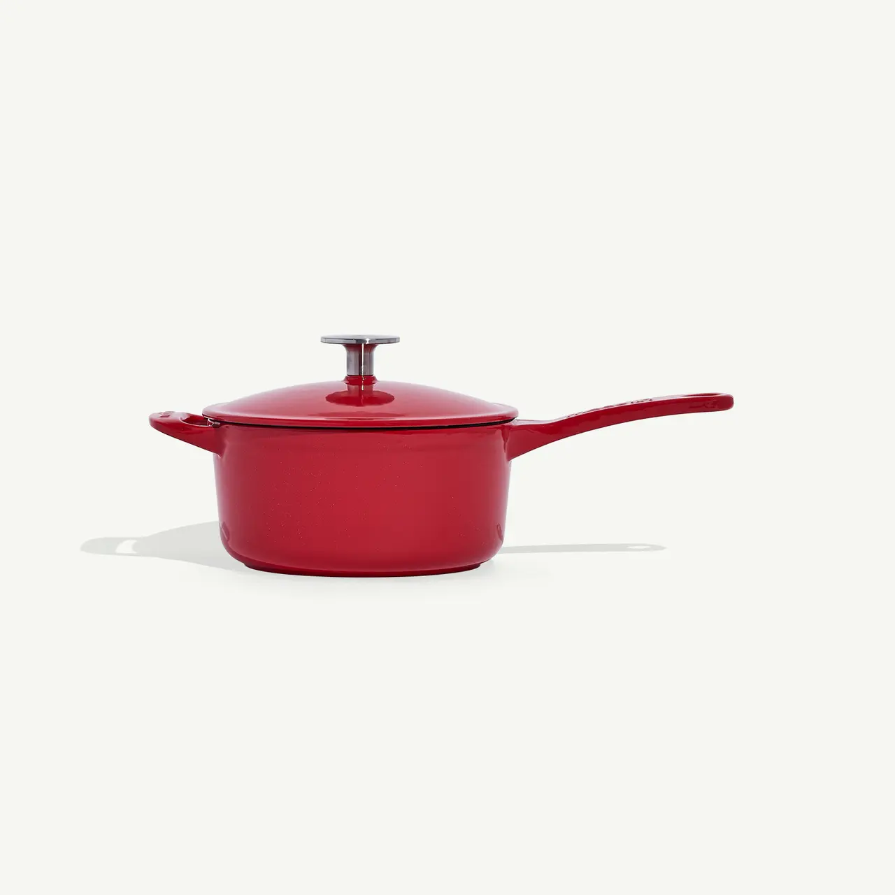 A red saucepan with a matching lid and a long handle is centered on a plain white background.