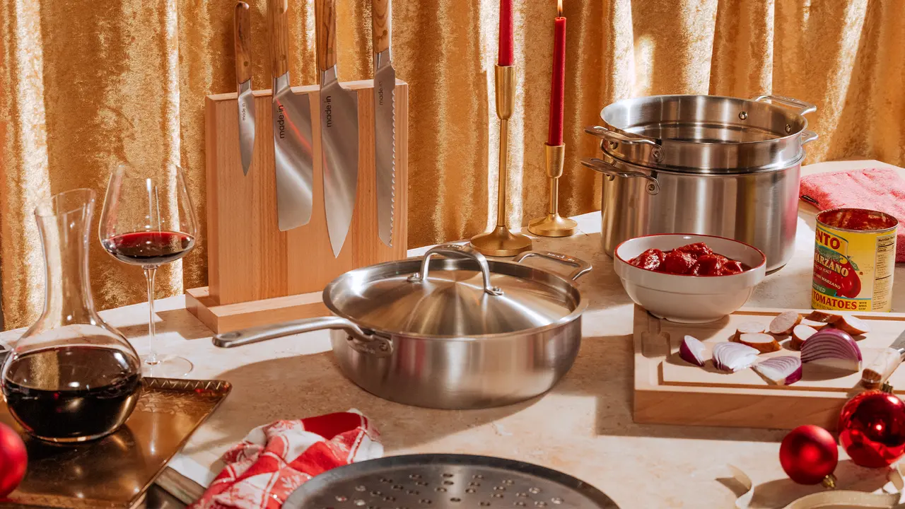 A festive cooking scene with stainless steel pots, a knife block, red wine glasses, and Christmas decorations on a gold glittery background.
