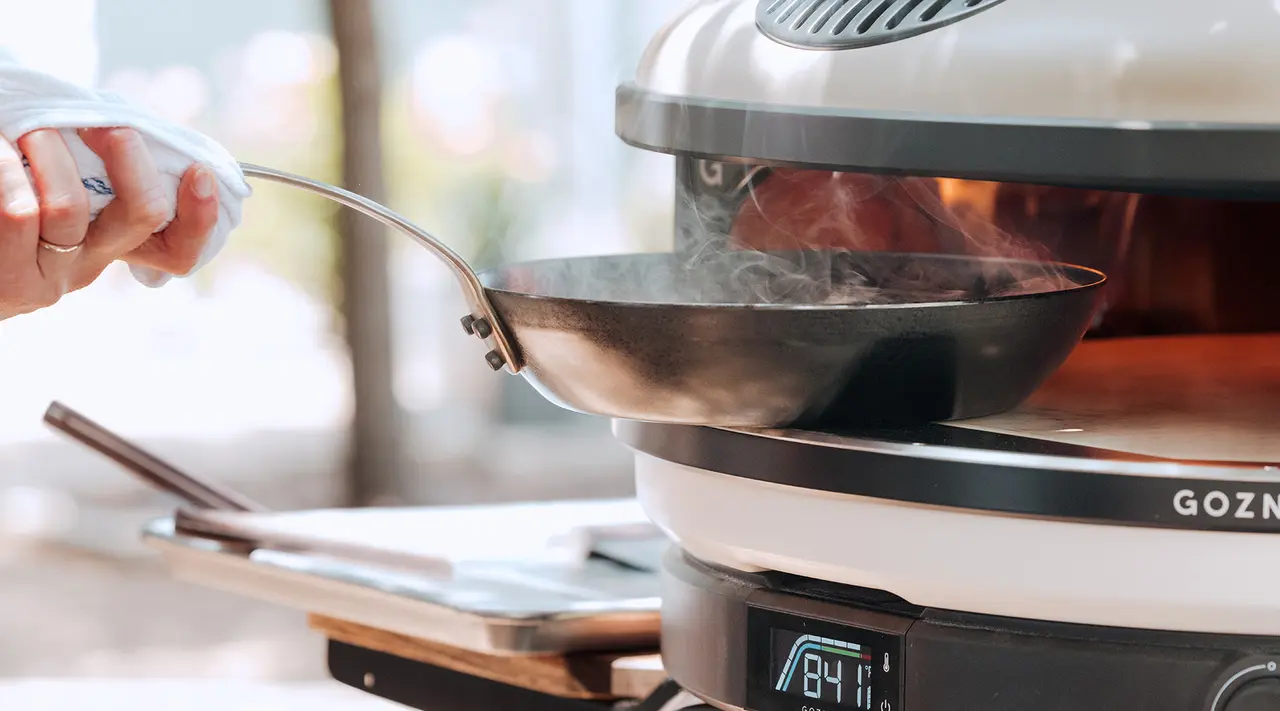 A person is cooking with a wok on a modern electric stove with a visible temperature reading of 84 degrees.