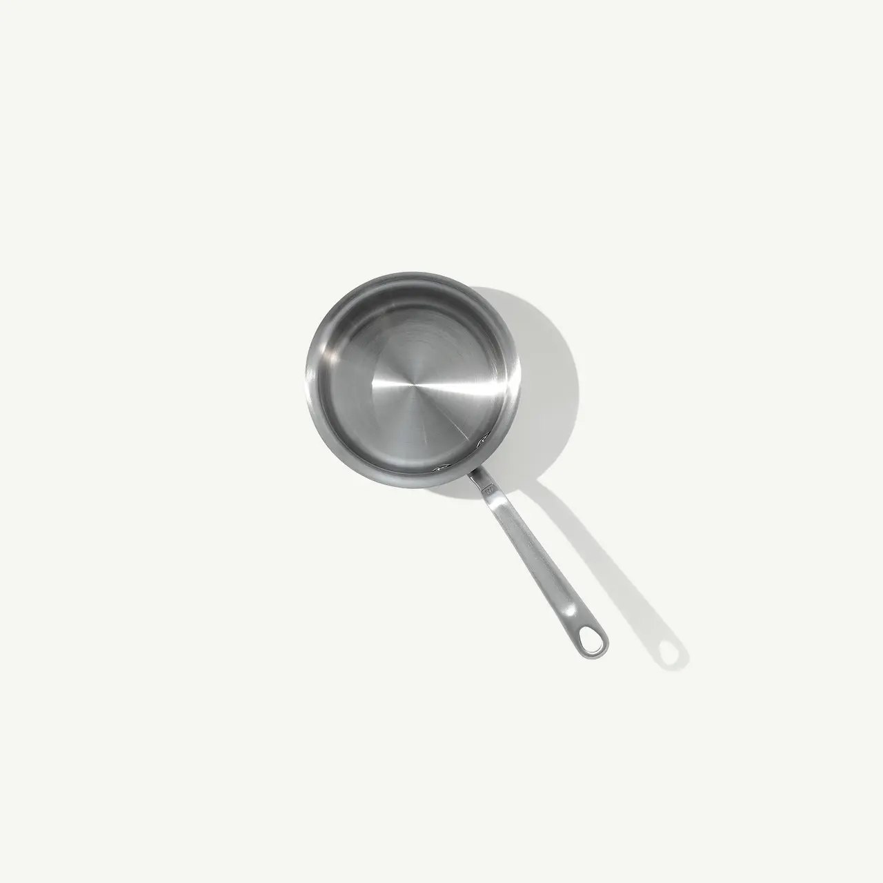 A stainless steel saucepan is centrally placed on a light background, casting a soft shadow beneath it.