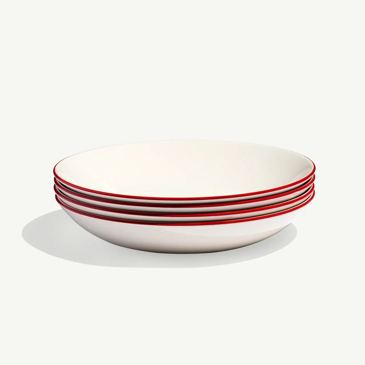 A stack of white bowls with red trim on a neutral background.