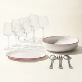 A set of elegant dinnerware consisting of plates, a bowl, cutlery, and wine glasses organized neatly on a light surface.