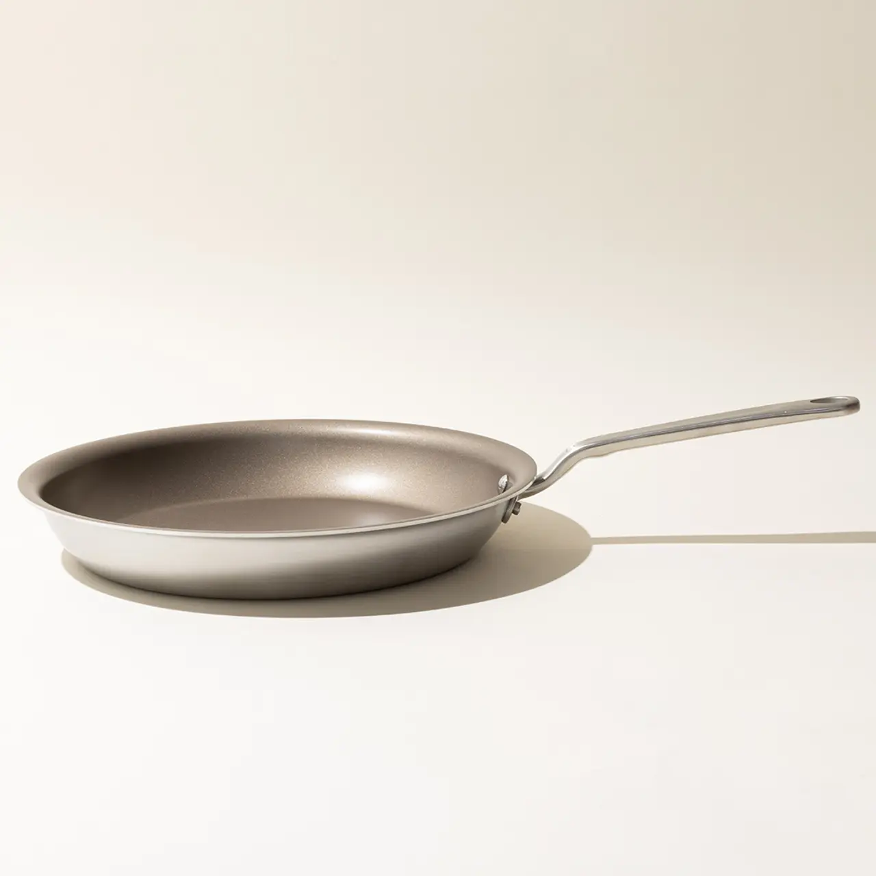 A non-stick frying pan with a long handle is placed on a neutral background, casting a slight shadow.