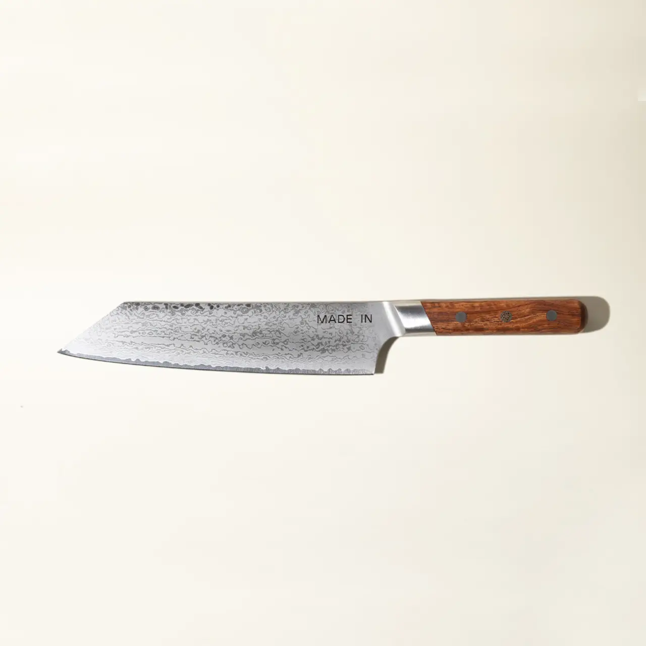 A Japanese chef's knife with a patterned blade and a wooden handle lies against a pale background.