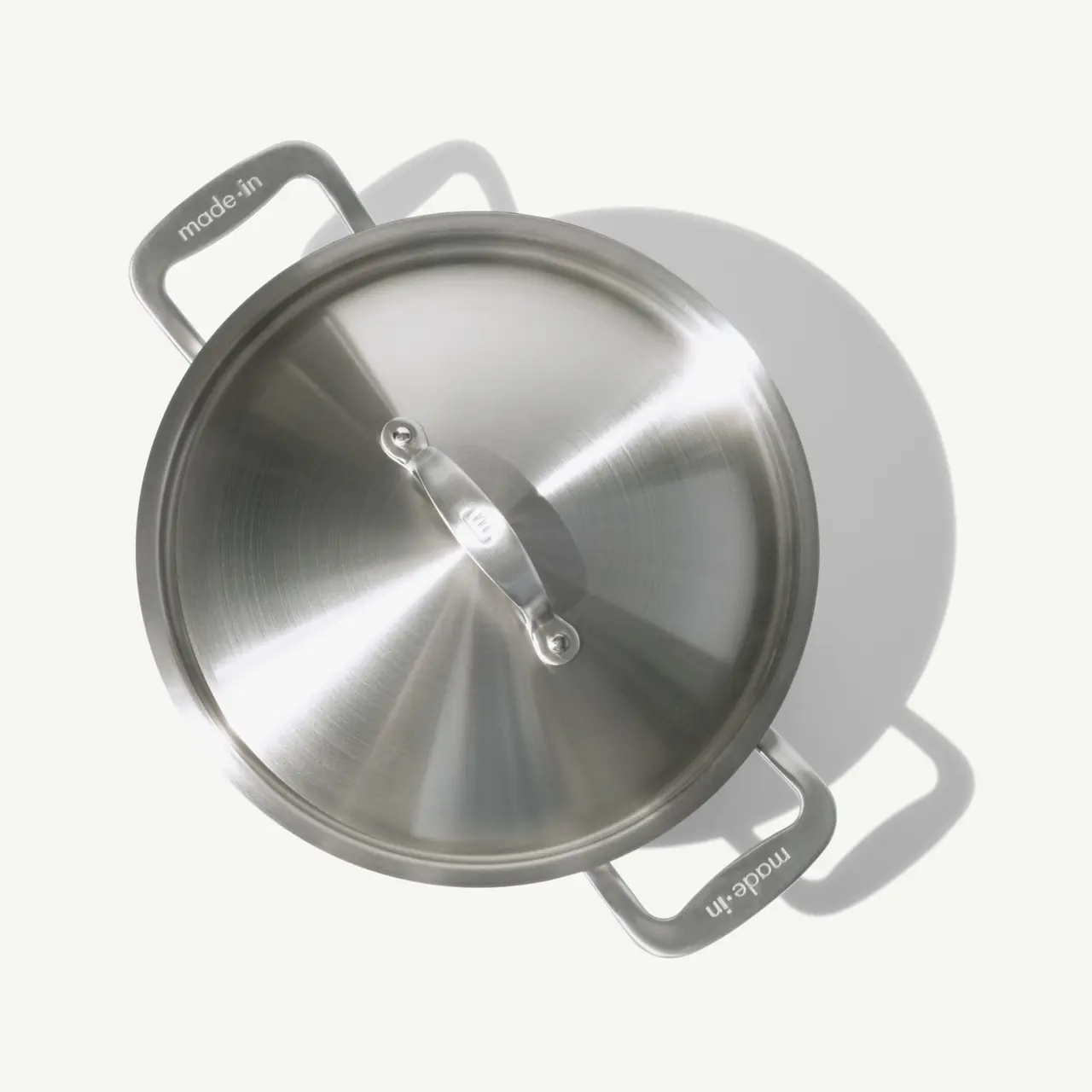 A stainless steel pot with its lid on is casting a soft shadow on a light surface.