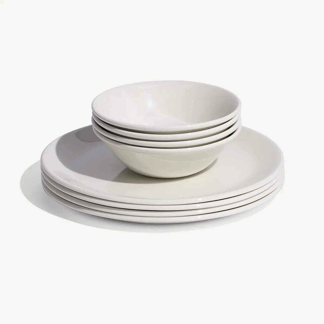 A stack of clean, white plates and bowls are neatly arranged on a light background.