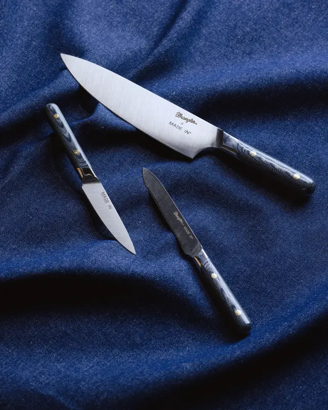 Three kitchen knives are elegantly arranged on a rich blue fabric backdrop.