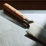 A detailed kitchen knife with a wooden handle rests on a stainless steel surface, showcasing its intricate blade design.