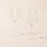 Two empty wine glasses stand side by side on a neutral background, casting soft shadows.