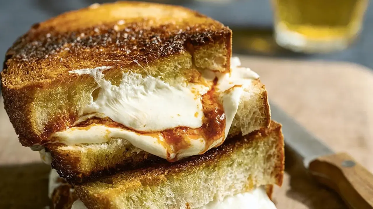 A golden-brown grilled cheese sandwich stacked with gooey melted cheese and tomato filling.