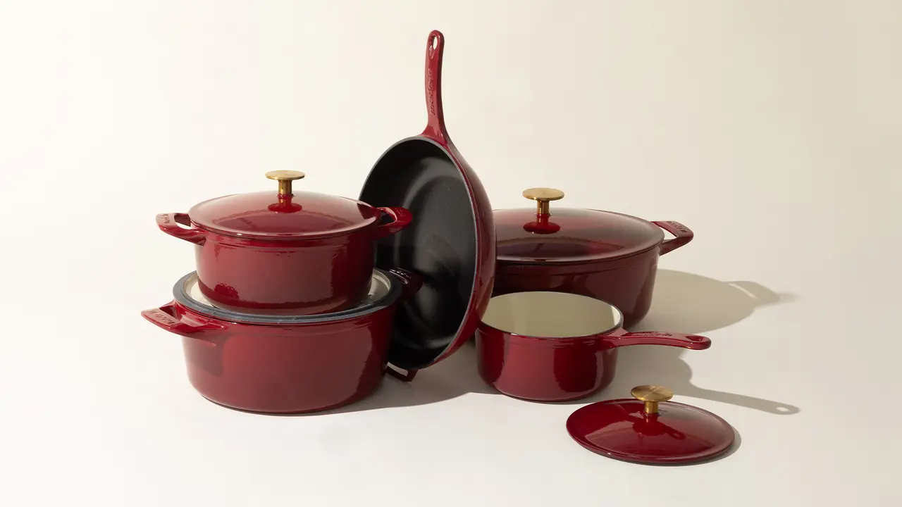 A collection of red cookware with lids, including pots and a frying pan, arranged neatly against a light background.