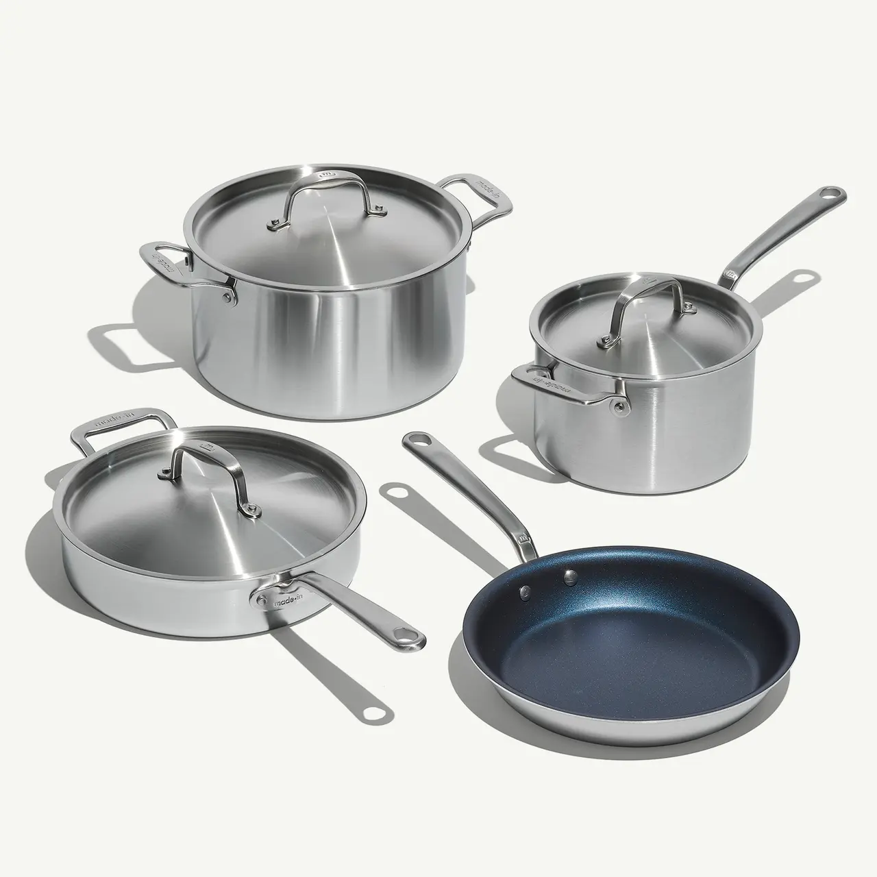 A set of stainless steel cookware with lids and a non-stick skillet on a light background.