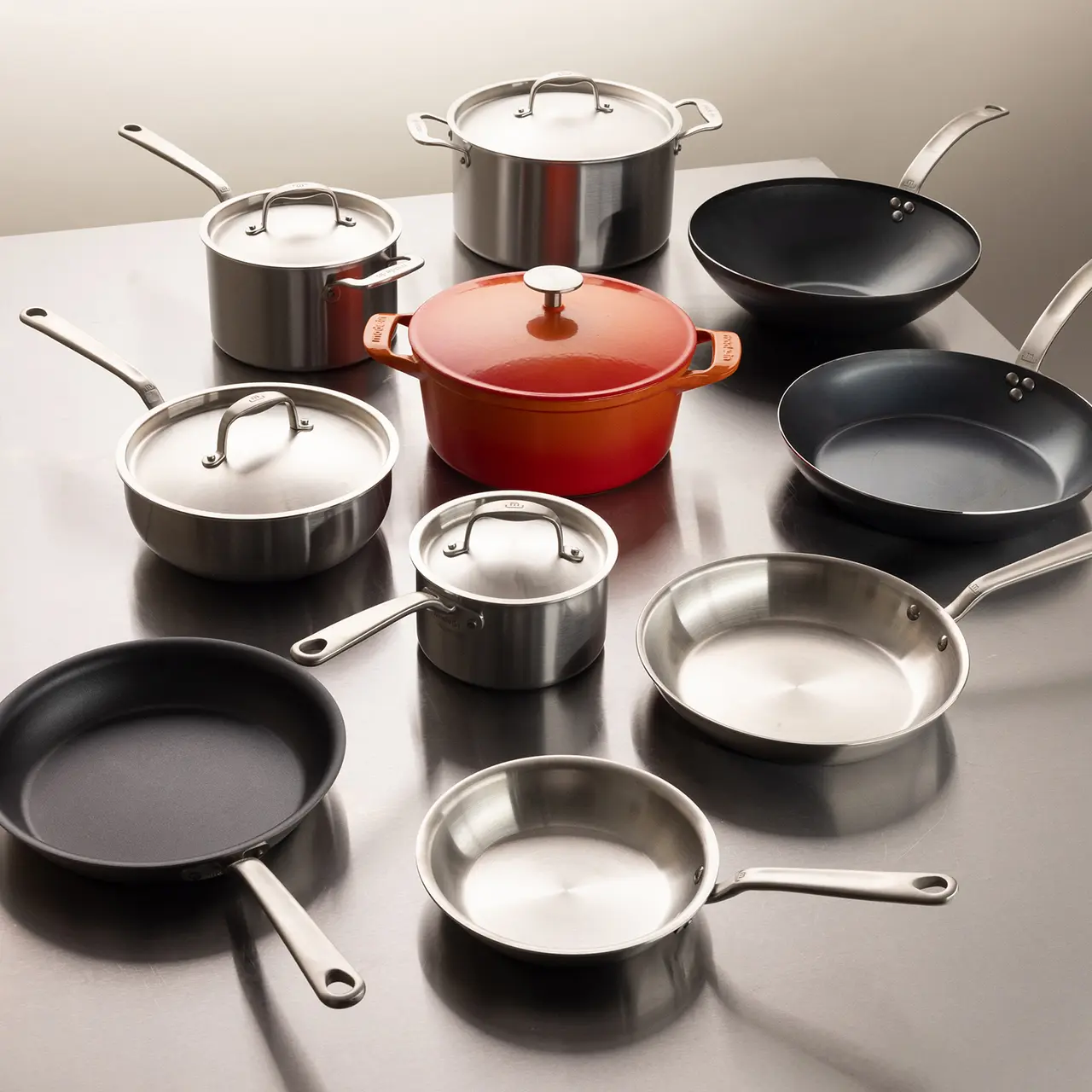 A collection of new cookware including pots, pans, and a red Dutch oven is neatly arranged on a kitchen counter.