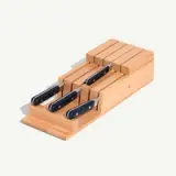 A wooden knife block holds a set of knives with black handles, arranged diagonally on a light background.