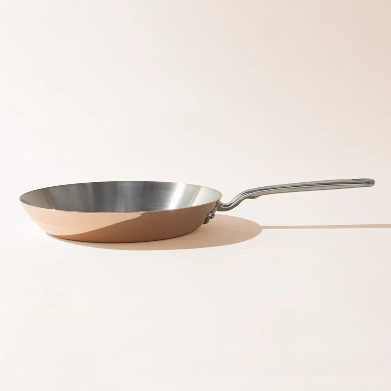 A stainless steel frying pan casts a long shadow on a light background.