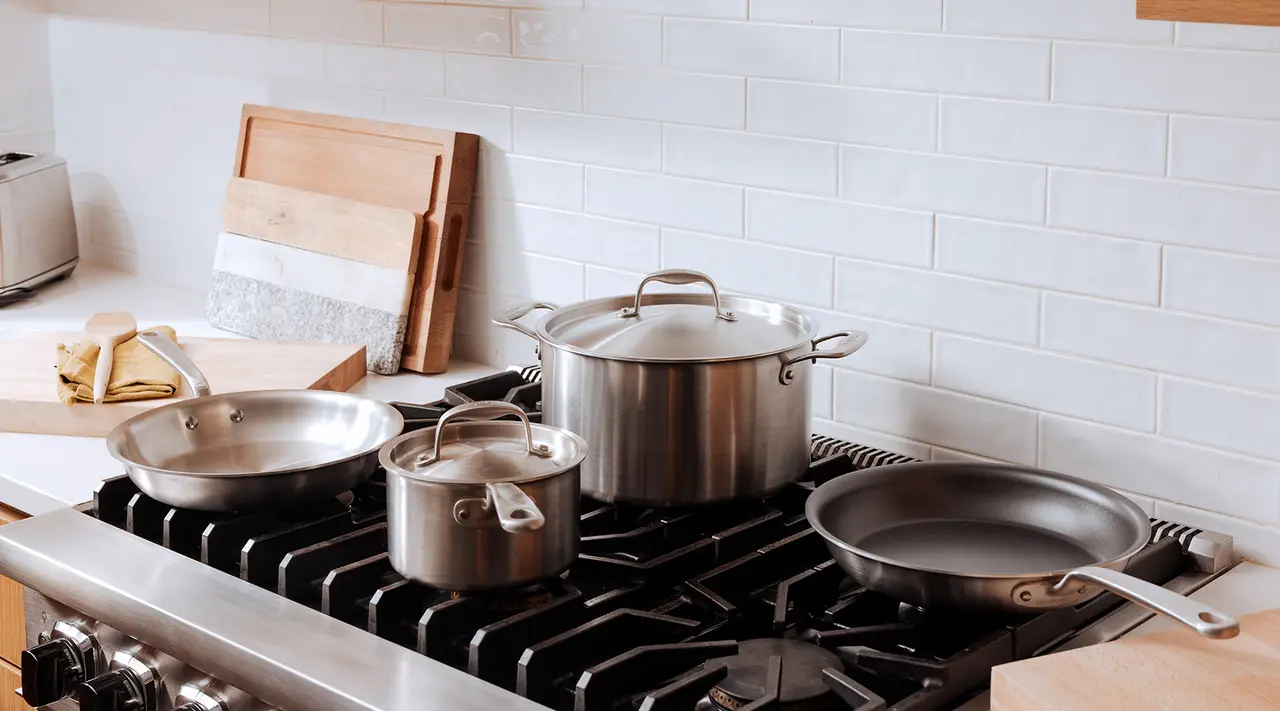 A variety of pots and pans are neatly arranged on a stove top in a kitchen with white tiled backsplash.