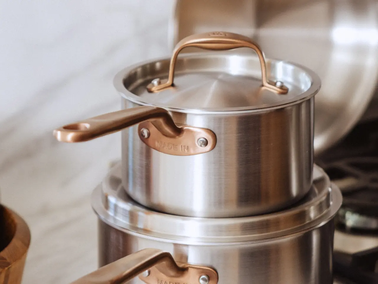 A stainless steel cooking pot with a copper handle sits atop another pot on a kitchen countertop.