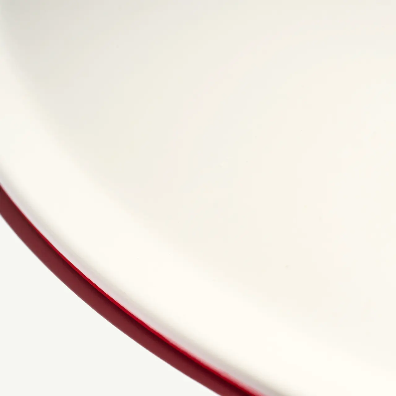 A close-up view of a white plate with a red rim on a plain background.