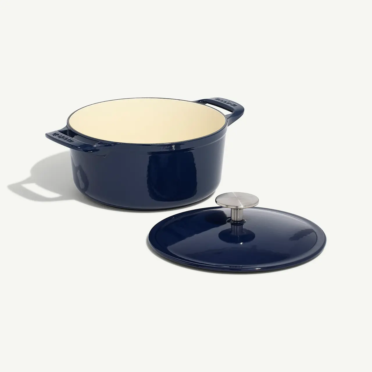 A navy blue enameled Dutch oven with its lid placed to the side on a light background.