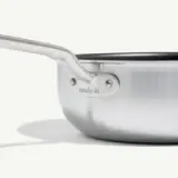 A close-up view of a stainless steel pan with a long handle, showing the brand "made-in" etched near the handle attachment.
