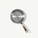 A stainless steel frying pan with a copper handle is shown from a top-down perspective.