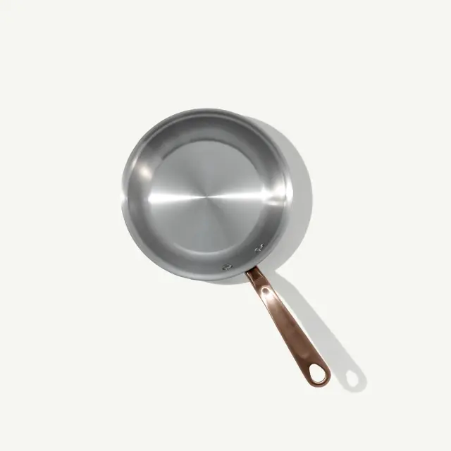 A stainless steel frying pan with a copper handle is shown from a top-down perspective.