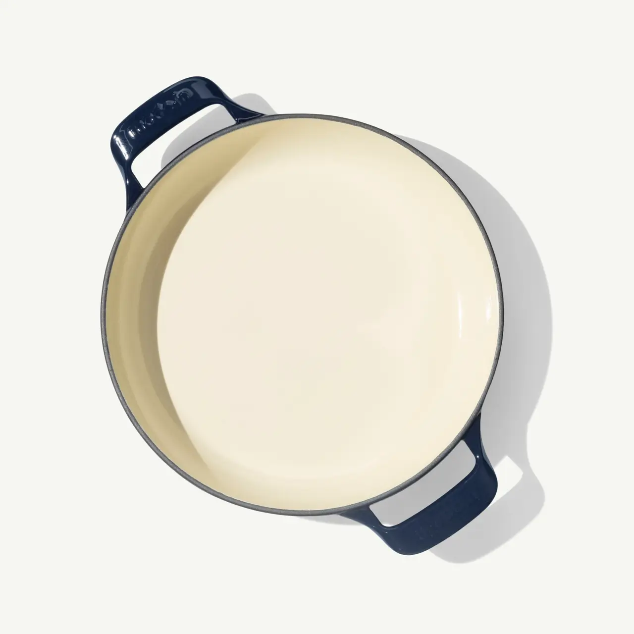 A round, enameled cast iron pot with a dark blue exterior and a cream-colored interior, viewed from above.