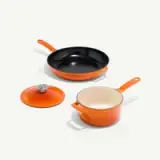 A set of orange cookware, including a frying pan, saucepan with a lid, and a pot, is arranged on a light background.