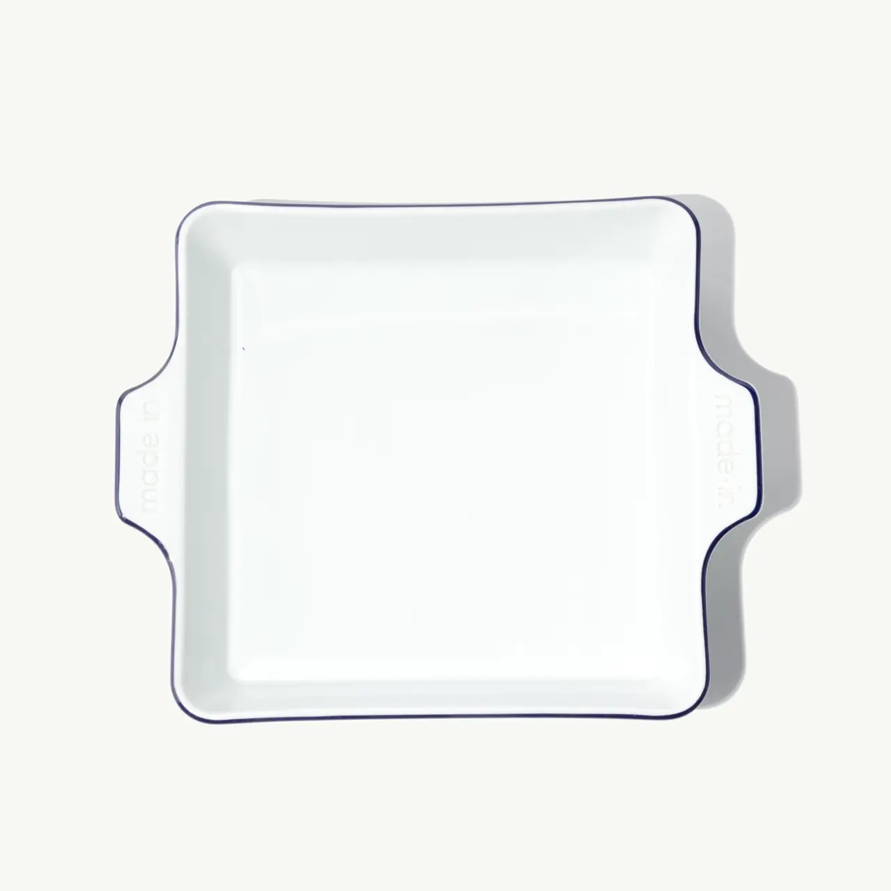 A square white ceramic dish with scalloped edges sits on a light background.