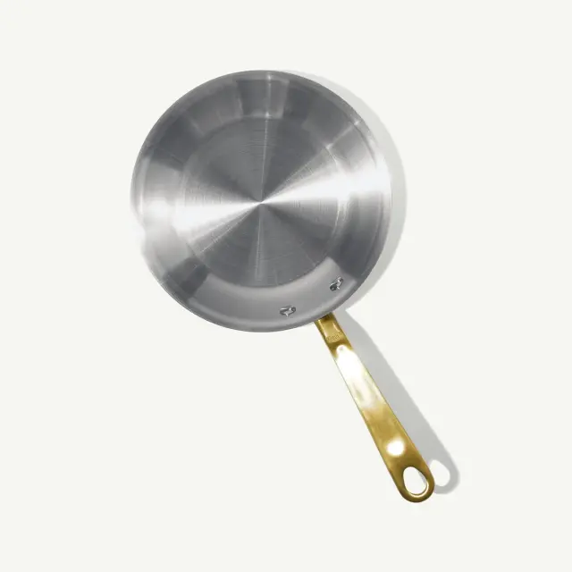 A stainless steel frying pan with a gold-colored handle against a light background.