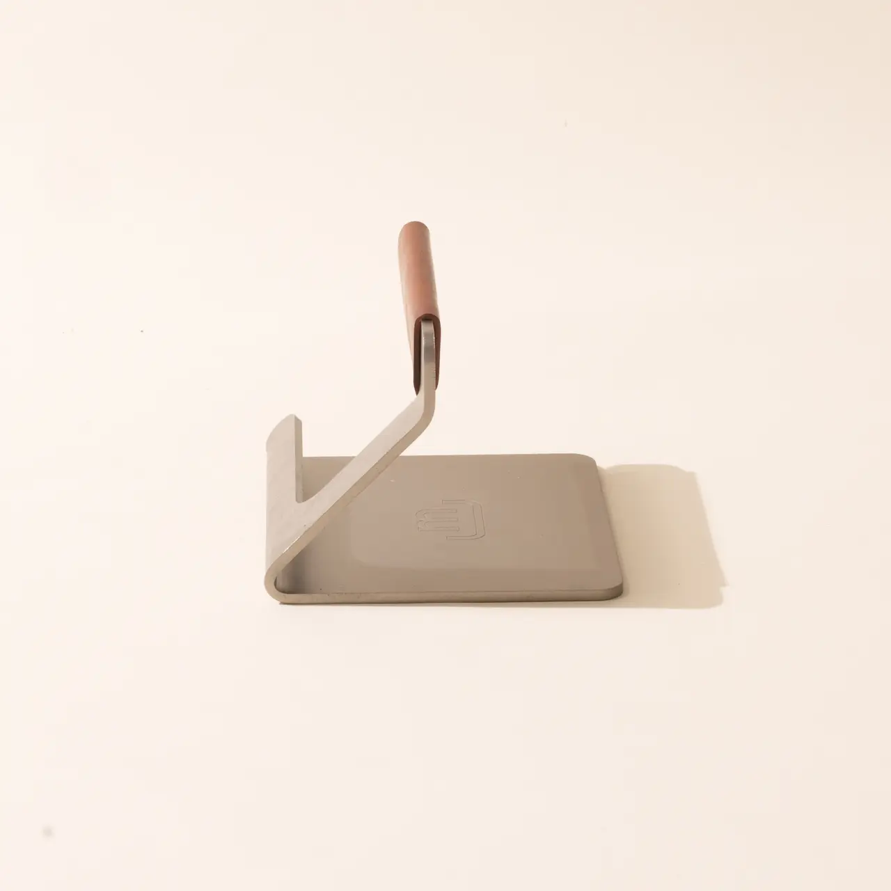 A metal dustpan with a wooden handle is leaning against a pale wall on a beige surface.
