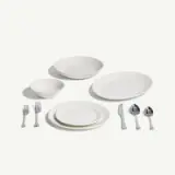A set of white dinnerware including two bowls, three plates, and cutlery arranged neatly on a light background.