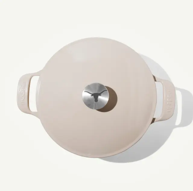 A round, beige enameled cast iron Dutch oven with a silver knob on the lid.