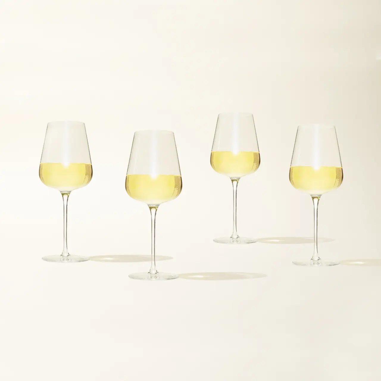 Four wine glasses filled with white wine are lined up on a light background.
