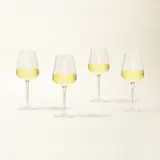 Four wine glasses filled with white wine are lined up on a light background.