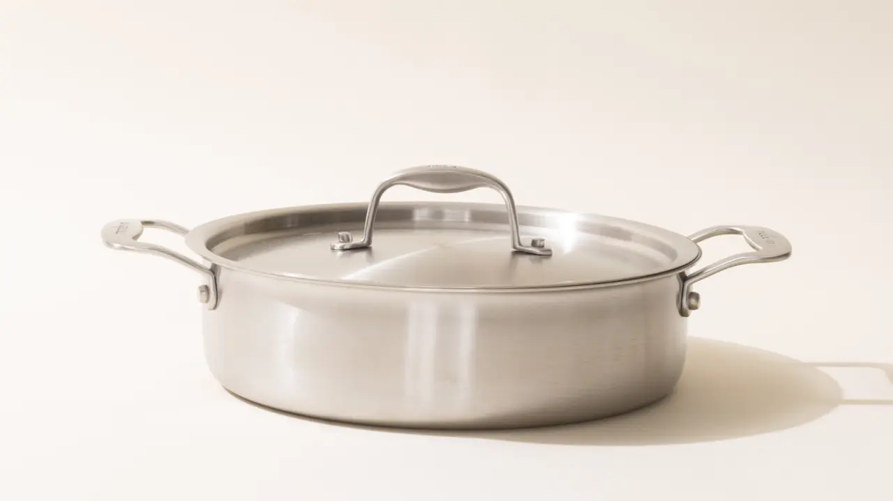 A stainless steel cooking pot with a lid on a light background.