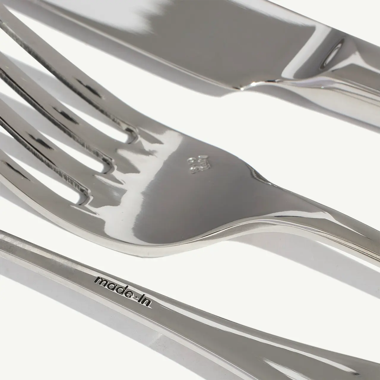 Two shiny silver forks lie on a white surface, reflecting light with a text "made in" visible on one of the handles.