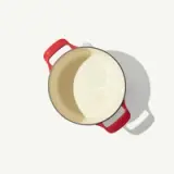 A red-handled, white enameled pot casts a shadow on a bright surface.