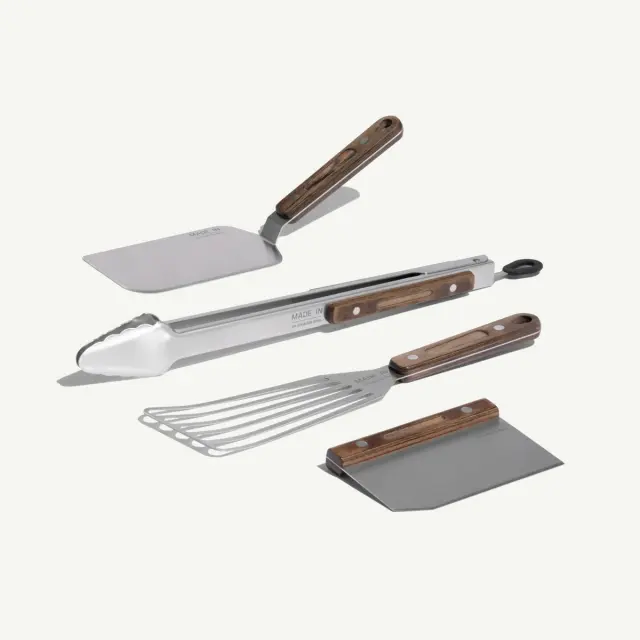 A set of four stainless steel cooking utensils with wooden handles, including a spatula, tongs, a grill scraper, and a turner.
