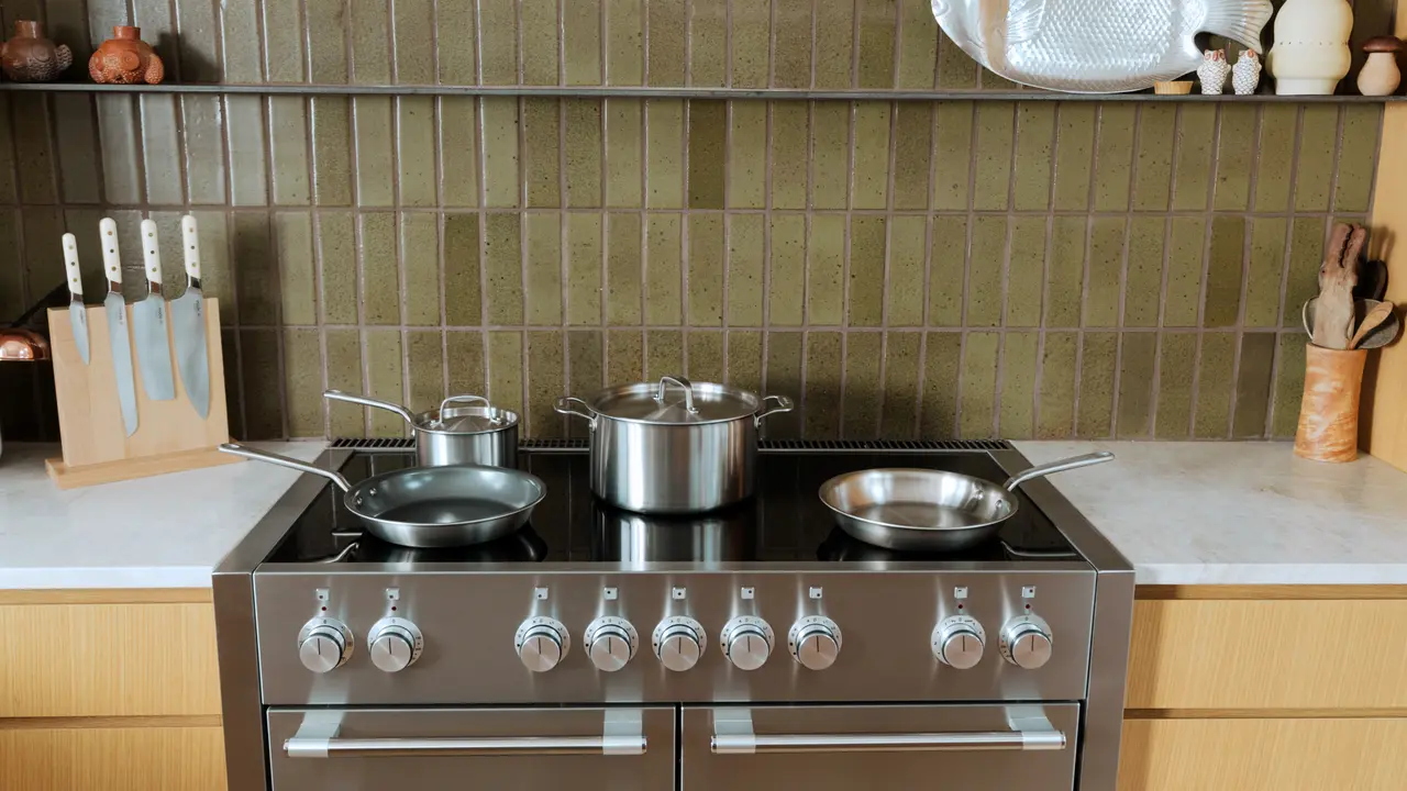 A modern kitchen stove top with pots and a pan, flanked by a knife block and cooking utensils, set against a tiled backsplash.