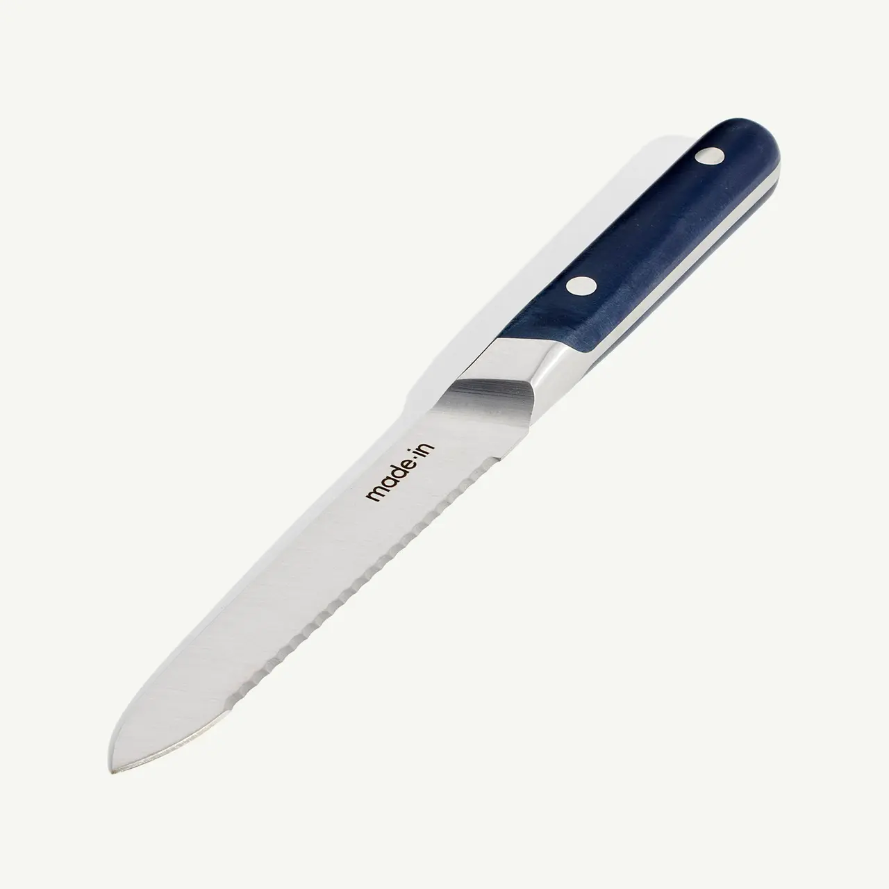 A kitchen knife with a serrated edge and a navy blue handle lies isolated against a white background.