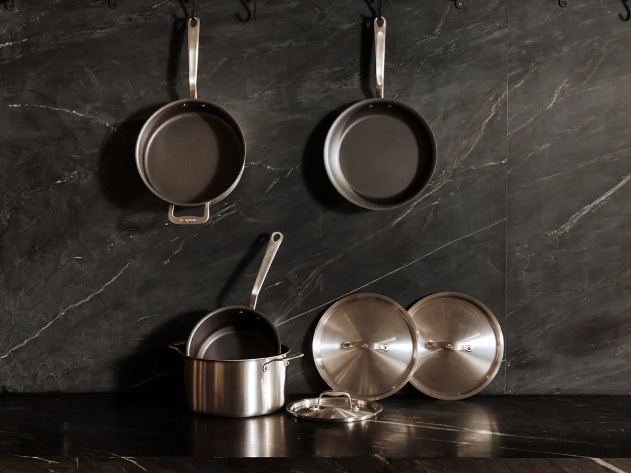 Several pots and pans are neatly arranged against a dark marble backdrop.